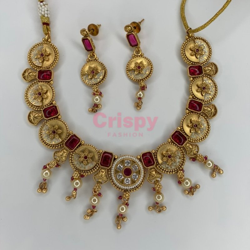 An antique gold-plated necklace and earring set featuring traditional Meena work, likely with red and white stone accents.