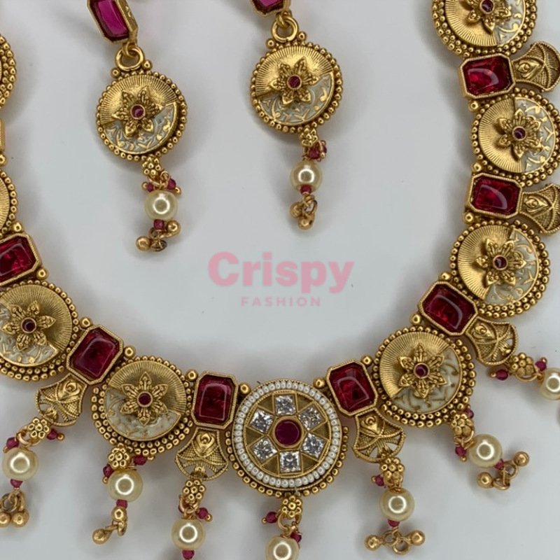 An antique gold-plated necklace and earring set featuring traditional Meena work, likely with red and white stone accents.